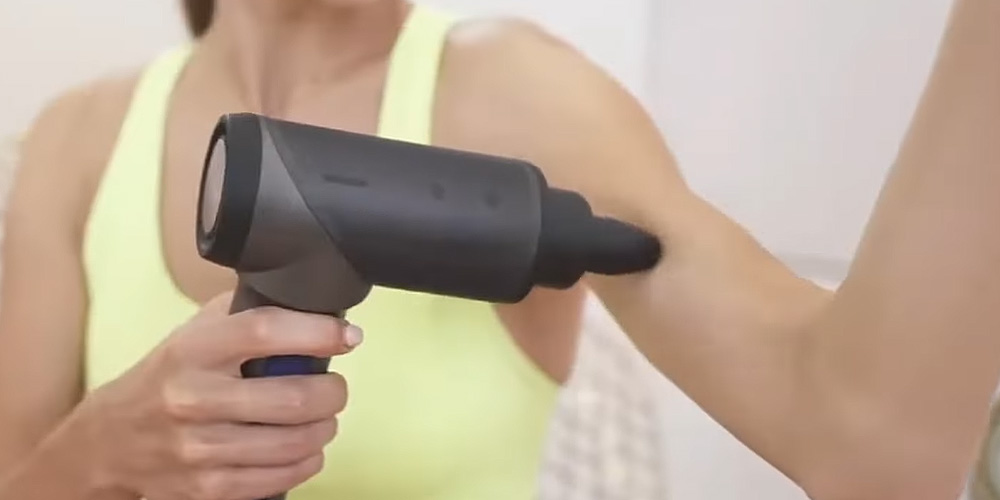 A woman using a massage gun on her arm 